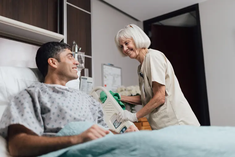 Environmental services associate talking with a smiling patient in bed