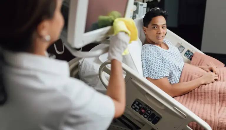 Young male patient smiles at nurse while sitting in hospital bed during interaction
