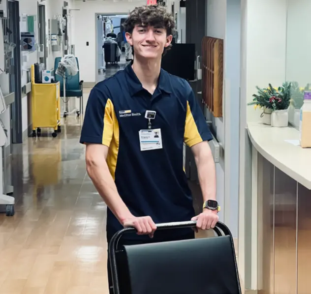 Smiling patient transporter pushing a wheelchair down a hospital corridor