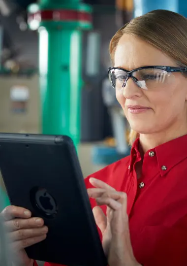 Facilities technician in safety glasses reviewing equipment data on a tablet