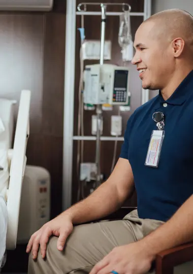 Patient sitter in a navy uniform seated at a patient’s bedside